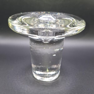 Puede incluir: Un portavelas de vidrio transparente con una parte superior ancha y plana y una base cilíndrica. El vidrio tiene un ligero tinte verdoso y parece soplado a mano. El diseño es simple y elegante, adecuado para varios estilos de decoración.