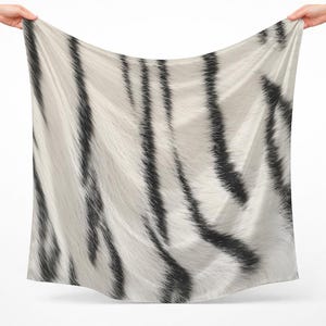 Puede incluir: Un pañuelo cuadrado con una base de color blanco y un patrón repetitivo de rayas negras verticales. La tela muestra una apariencia texturizada que imita el aspecto del pelaje animal, con pliegues suaves y fluidos creados al sostener la tela.