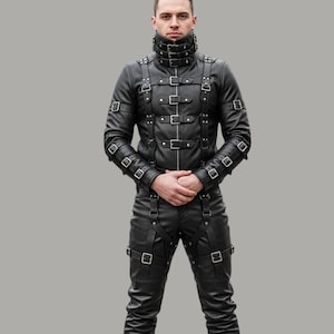 Puede incluir: Conjunto de chaqueta y pantalón de cuero negro con múltiples correas, hebillas y cuello alto. La chaqueta tiene cierre de cremallera y el pantalón tiene correas alrededor de los muslos. El conjunto está diseñado con una estética única y atrevida.