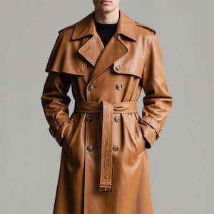 May include: A brown leather trench coat with a double-breasted design, a belt, and a classic collar. The coat features a shoulder cape and pockets. The coat is a medium brown color.