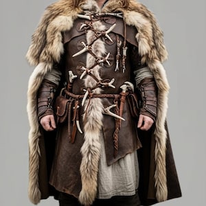 May include: A brown leather and fur costume with a fur-lined cape. The costume features bone accents, a braided belt, and leather arm cuffs. The outfit has a medieval or fantasy theme.