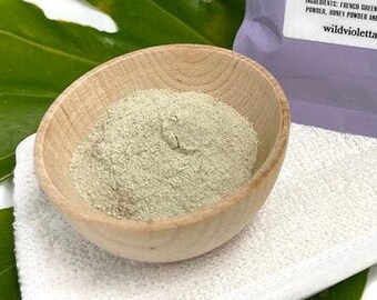 May include: A purple pouch with a white label that reads "wild violetta CLAY FACE MASK milk & honey". The label describes the benefits of using the clay mask. The pouch is sitting on a white towel and green leaves.