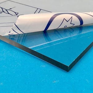 May include: A close-up of a blue sheet of material with a protective film partially peeled back. The material has a black edge and is on a blue surface. The film has a blue and white design.