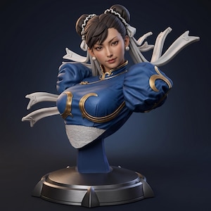 Op de afbeelding: Een borstbeeld van een personage met donker haar in twee knotjes met witte linten. De figuur draagt een blauw kledingstuk met een hoge kraag, gouden biezen, pofmouwen en een wit kanten detail bij de taille, op een ronde metalen voet.