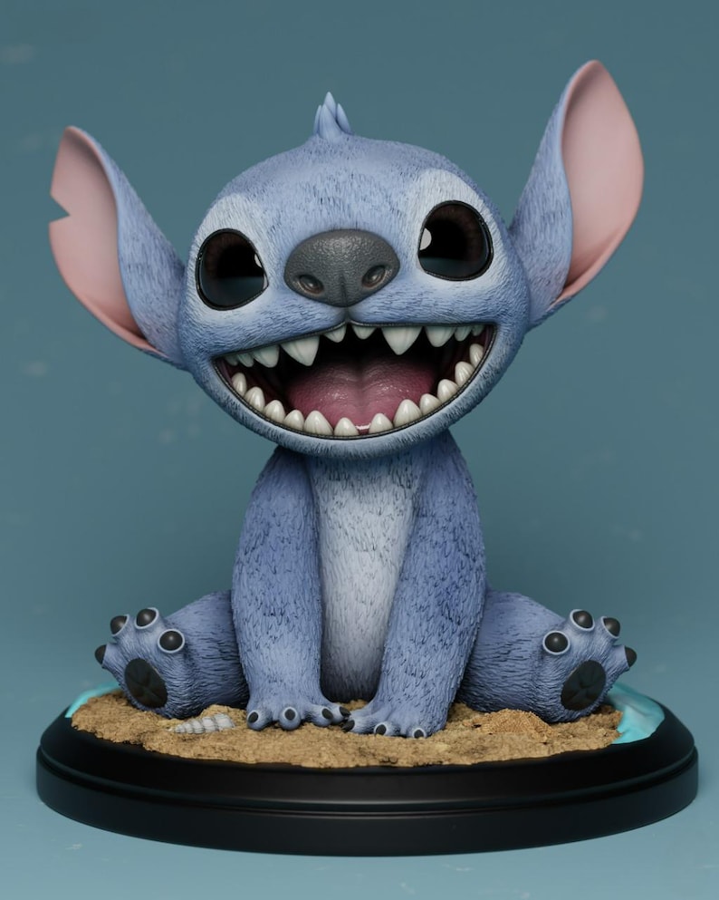 Puede incluir: Figura de Stitch azul y peludo, con grandes ojos expresivos y una amplia sonrisa que muestra dientes afilados. La figura est&aacute; sobre una base arenosa, a su vez sobre un soporte negro circular. Las orejas son rosas por dentro.