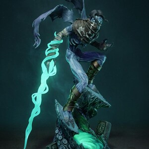 May include: A detailed figurine of a character with blue skin, dark hair, and a mask. The figure is posed dynamically, with a glowing teal energy stream emanating from its arm. It stands on a detailed, rocky base with a glowing green pool.