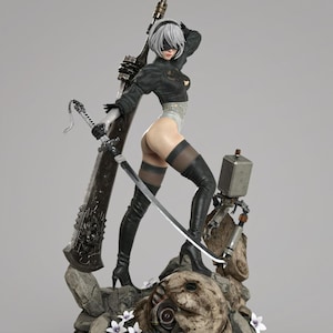 May include: A detailed figurine of a character with short white hair and a black blindfold, wearing a black long-sleeved top, white leotard, and black thigh-high boots. The figure holds a long sword and stands on a rocky base with small white flowers.