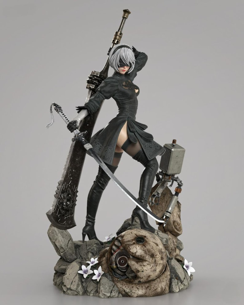 May include: A detailed figurine of a character with short white hair, a black blindfold, and a black dress with lace details. The figure holds a large sword and stands on a rocky base with small white flowers and a small mechanical robot companion.