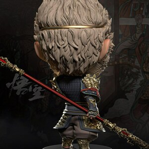 May include: A detailed figurine of a monkey-like character in traditional armor, holding a red and gold staff. The figure has a textured, light-colored fur-like head and is posed on a black base. The armor is detailed with gold accents.
