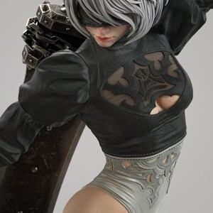 May include: A detailed figurine of a character with short silver hair and a black blindfold. The figure wears a black long-sleeved top with a decorative cutout chest panel and a light gray leotard with intricate cutouts, carrying a large dark sword.