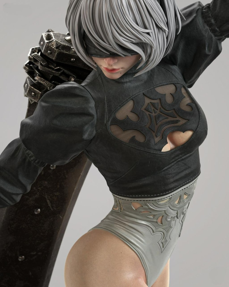 May include: A detailed figurine of a character with short silver hair and a black blindfold. The figure wears a black long-sleeved top with a decorative cutout chest panel and a light gray leotard with intricate cutouts, carrying a large dark sword.