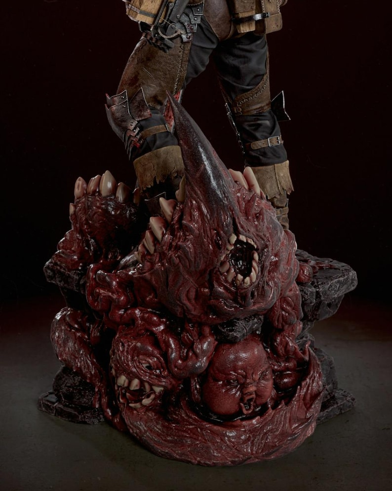 May include: A detailed collectible figurine base featuring a cluster of grotesque, fleshy, dark red organic masses with sharp teeth and a small, distorted face. The base supports the lower legs of a figure wearing brown leather and black trousers.