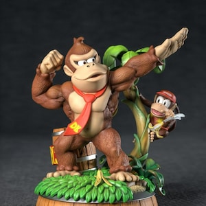 May include: A detailed figurine of Donkey Kong flexing his muscles, wearing a red tie with "DK" on it. A smaller monkey figure is perched on a tree branch. The base is a wooden barrel design with green foliage and a banana.