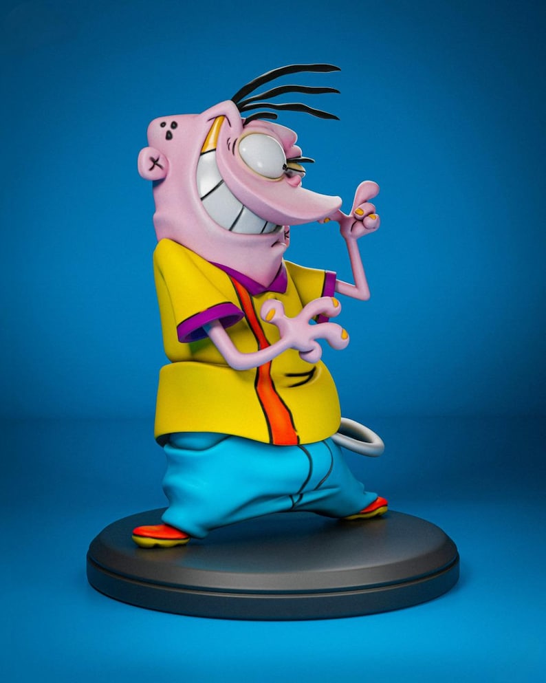 May include: A figurine of the cartoon character Ed from Ed, Edd n Eddy. The figure is posed with a wide grin, wearing a yellow shirt with purple trim, blue pants, and orange shoes. The figure is on a black circular base against a blue background.