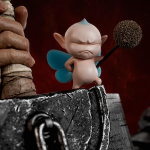 May include: A small, pale pink fairy figurine with pointed ears, blue wings, and a grumpy expression, holding a brown, spherical, textured staff. The figure stands atop a large, weathered, dark gray metallic hammer with a prominent iron ring.