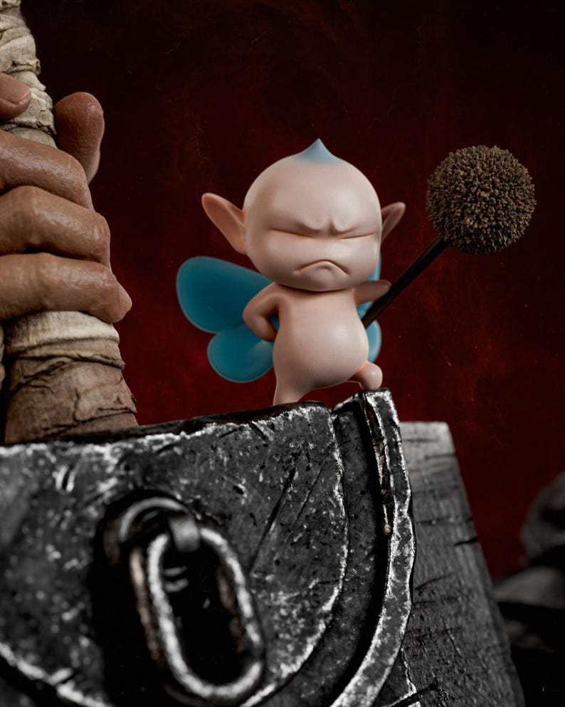 May include: A small, pale pink fairy figurine with pointed ears, blue wings, and a grumpy expression, holding a brown, spherical, textured staff. The figure stands atop a large, weathered, dark gray metallic hammer with a prominent iron ring.
