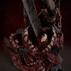 May include: A detailed collectible statue featuring a dark, weathered sword blade piercing a grotesque, fleshy base covered in numerous human-like teeth and bloodshot eyes. The figure wears dark trousers and armored boots, standing atop the mass.
