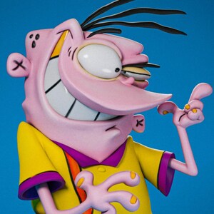 May include: A figurine of a cartoon character with pink skin, a large nose, and a wide grin. The character wears a yellow shirt with purple trim and has black hair. The background is a solid blue.
