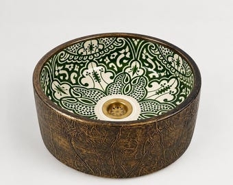 May include: A round vessel sink featuring a dark, textured bronze-toned exterior and an interior decorated with a green and white floral pattern. The basin includes a central brass-colored drain fixture with a circular perforated design.
