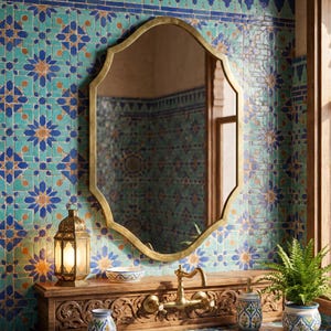 Handmade Moroccan brass arch wall mirror above a carved wooden vanity, featuring an antique brass frame inspired by Moorish architecture, styled with blue Moroccan zellige tiles, brass faucet, ceramic accessories, and traditional lantern.