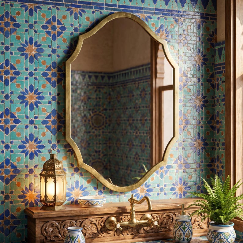 Handmade Moroccan brass arch wall mirror above a carved wooden vanity, featuring an antique brass frame inspired by Moorish architecture, styled with blue Moroccan zellige tiles, brass faucet, ceramic accessories, and traditional lantern.