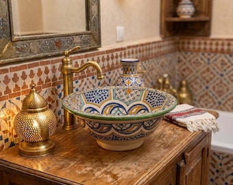 May include: A decorative bathroom sink with a colorful geometric pattern in blue, yellow, and green. The sink sits on a wooden cabinet with a brass faucet. A gold lantern and a decorative vase are also visible.