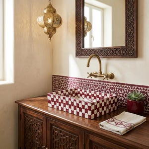 May include: A rectangular ceramic sink with a red and white scalloped pattern sits on a dark wood vanity. Above it, a wall-mounted brass faucet, a mirror with a carved wooden frame, and a hanging brass pendant light with intricate cutouts.