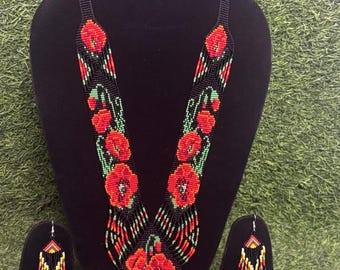 May include: A beaded necklace and earring set featuring a floral design. The necklace and earrings are primarily black with red and green floral accents. The necklace has a long, fringed pendant.