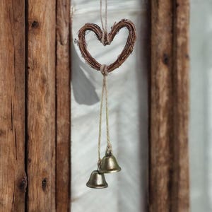 Peut inclure: Décoration en forme de cœur rustique, faite de brindilles tressées, suspendue par une ficelle naturelle. Deux petites cloches en laiton antiques pendent en dessous. Fond avec un cadre en bois et un rideau blanc.