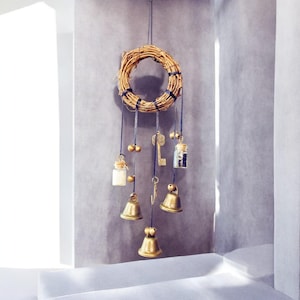 Könnte beinhalten: Dekorative Hängemobile mit einem geflochtenen Kranz und dunkelblauen Bändern. Das Mobile umfasst kleine Glasflaschen, Messingglocken und antike Schlüssel. Die Glocken und Schlüssel sind an dem Kranz aufgehängt.