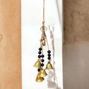 Pode incluir: Enfeite decorativo suspenso com pequenos sinos de latão, contas pretas e chaves de estilo antigo. Os sinos são suspensos por um cordão de fio natural, criando uma estética rústica. Para decoração de interiores.