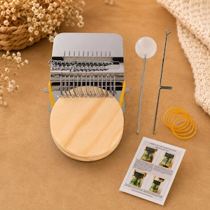 May include: A small metal darning loom with a round wooden base, featuring a series of silver hooks. Included are a long metal needle with a white spherical top, a thin metal hook tool, several yellow rubber bands, and an instruction card.