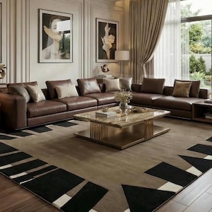 May include: A large rectangular area rug featuring a taupe center with a geometric border pattern of black and white triangles and rectangles. The rug is positioned on a wooden floor in a living room with a brown leather sectional sofa and coffee table.