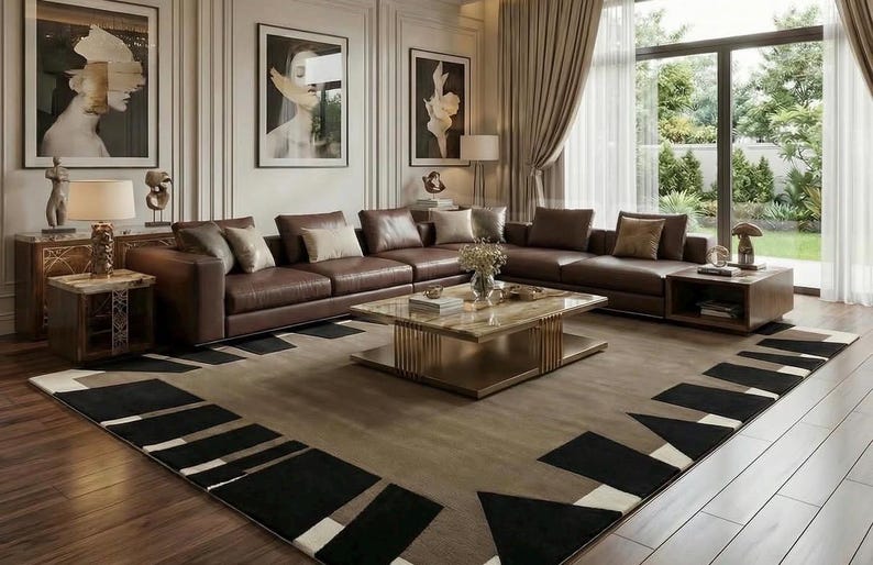 May include: A large rectangular area rug featuring a taupe center with a geometric border pattern of black and white triangles and rectangles. The rug is positioned on a wooden floor in a living room with a brown leather sectional sofa and coffee table.