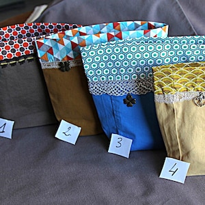 May include: Four fabric storage bags with patterned tops and solid-colored bodies. The bags have different designs: red and white polka dots, blue and white triangles, green hexagons, and yellow fan shapes. Each bag has a decorative trim and a small charm.