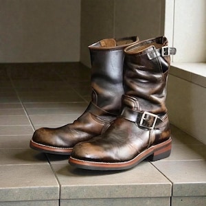 Puede incluir: Un par de botas de cuero marrones para motocicleta con hebillas. Las botas tienen un aspecto desgastado, con pliegues y variaciones de color. Las suelas son de color marrón contrastante con un borde más claro.