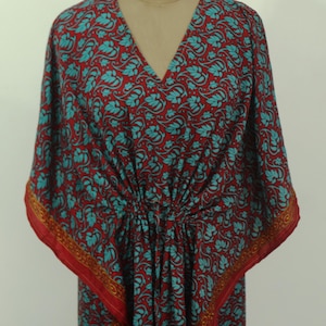 Könnte beinhalten: Ein Kaftan-Kleid mit tiefroter Grundfarbe und einem sich wiederholenden Muster aus türkisfarbenen Blättern und Ranken. Das Kleidungsstück hat einen V-Ausschnitt, weite Kimono-Ärmel und eine geraffte Taille mit vertikalen Falten.