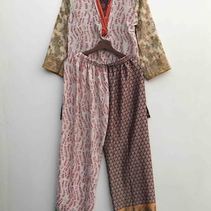 Könnte beinhalten: Ein zweiteiliges Pyjama-Set mit einem langärmeligen Oberteil und einer passenden Hose. Das Oberteil ist cremefarben mit roten wellenartigen Mustern und floralen Ärmeln. Die Hose ist geteilt, wobei eine Seite das gleiche Muster wie das Oberteil und die andere ein blaues und orangefarbenes Blumenmuster aufweist.