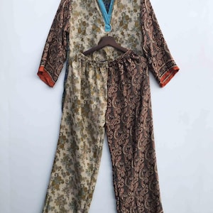 May include: A two-piece pajama set with a floral and paisley pattern. The top has long sleeves and a mandarin collar with a blue tie. The pants are split down the middle with two different patterns. The set is in shades of beige, brown, and orange.
