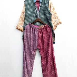 Könnte beinhalten: Ein zweiteiliges Set bestehend aus einem langärmeligen Hemd und einer passenden Hose. Das Hemd hat ein blaugrünes Oberteil mit Muster, einen hellblauen Kragen und cremefarbene Ärmel mit Blumenmuster. Die Hose ist in zwei Abschnitte unterteilt, einer mit violettem Paisley-Druck und der andere mit einem dunkelrosa Blumenmuster.
