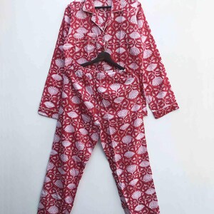 Könnte beinhalten: Rotes und weißes Pyjama-Set mit floralem Muster. Das langärmlige Oberteil und die Hose sind aus einem weichen Stoff gefertigt. Der Pyjama hängt an einem Holzbügel vor einem weißen Hintergrund. Das Set hat ein Oberteil zum Knöpfen mit Kragen und eine passende Hose.