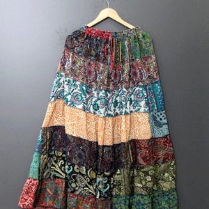 Könnte beinhalten: Langer Patchwork-Rock mit Paisley- und Blumenmustern in Rot, Blau, Grün und Orange. Der Rock hängt an einem Holzbügel vor grauem Hintergrund. Der Rock hat einen Kordelzug in der Taille. Der Rock ist etwa 90 cm lang.