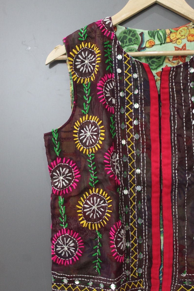 Puede incluir: Un chaleco marr&oacute;n con bordados florales coloridos. El chaleco presenta dise&ntilde;os de flores amarillas, rosas y blancas con tallos verdes. Tiene una raya roja en la parte delantera y est&aacute; decorado con peque&ntilde;os adornos plateados redondos.