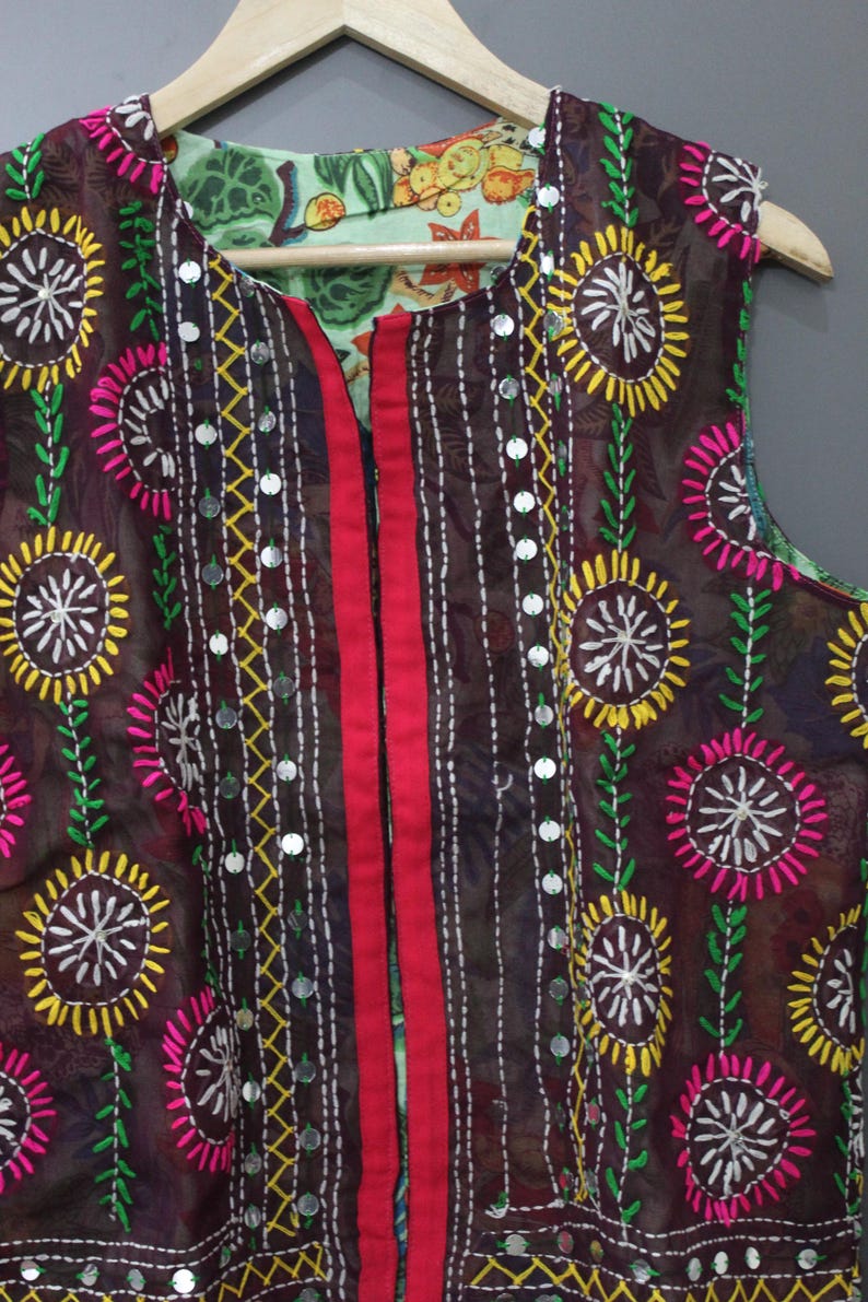 Puede incluir: Prenda reversible sin mangas con estampado floral. La capa exterior es marr&oacute;n con flores bordadas en amarillo, rosa y blanco. La capa interior tiene un estampado floral verde claro. Una franja roja recorre el centro.