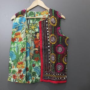 Puede incluir: Un chaleco colorido con estampado floral y de figuras. El chaleco presenta una variedad de colores, incluyendo verde, rojo, azul y marr&oacute;n. El chaleco est&aacute; colgado en una percha de madera sobre un fondo gris.