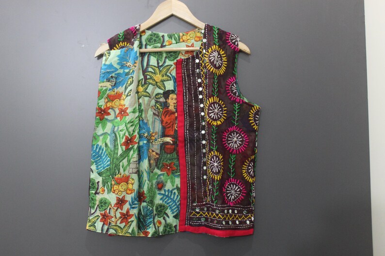 Puede incluir: Un chaleco colorido con estampado floral y de figuras. El chaleco presenta una variedad de colores, incluyendo verde, rojo, azul y marr&oacute;n. El chaleco est&aacute; colgado en una percha de madera sobre un fondo gris.