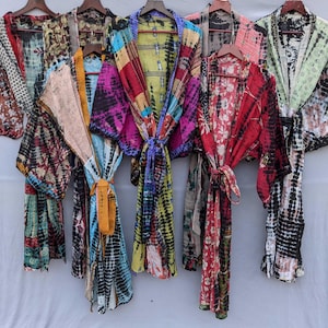 Könnte beinhalten: Eine Sammlung von sechs langärmeligen Morgenmänteln, die an Holzkleiderbügeln hängen. Jeder Morgenmantel weist ein einzigartiges Patchwork-Design mit verschiedenen Batikmustern, Blumenprints und geometrischen Motiven in leuchtenden Farben wie Rot, Blau, Gelb und Grün auf.