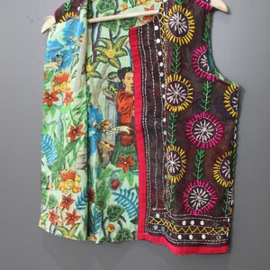 Puede incluir: Un chaleco sin mangas con un estampado floral y de figuras colorido. El chaleco presenta un panel bordado marr&oacute;n con detalles de espejo y un ribete rojo. El forro interior tiene un estampado floral verde y azul.