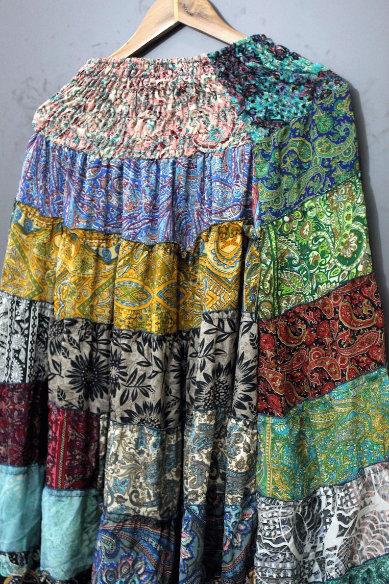 May include: A patchwork skirt with a variety of colourful patterns, including paisley, floral, and geometric designs. The skirt is made of multiple fabric panels in shades of blue, green, yellow, red, and black. The skirt is hanging on a wooden hanger.
