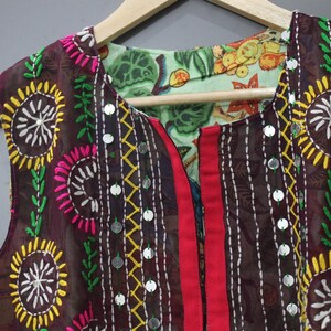 Puede incluir: Un chaleco marr&oacute;n sin mangas con bordados coloridos. El chaleco presenta dise&ntilde;os florales amarillos, rosas y blancos, detalles de hojas verdes y peque&ntilde;os adornos plateados. El chaleco es reversible, con un forro estampado floral.